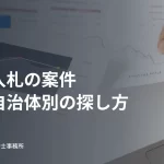 パソコンと紙の資料で情報を確認する手元。公共入札の案件の探し方の見出し入り