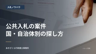 パソコンと紙の資料で情報を確認する手元。公共入札の案件の探し方の見出し入り