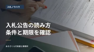 机上の書類を確認する人の手元。入札公告の条件と期限を確認する見出し入り