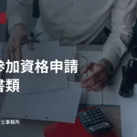デスクで書類を整理する人。入札参加資格申請の必要書類の見出し入り