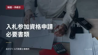 デスクで書類を整理する人。入札参加資格申請の必要書類の見出し入り
