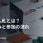 パソコンと書類が置かれた会議テーブル。公共入札の仕組みと参加の流れの見出し入り